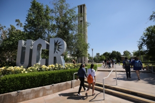 Students walk past a silver UCR letter sign.